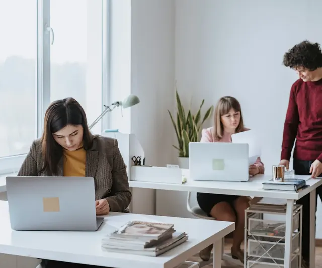 Three people working at desks in a bright, small office