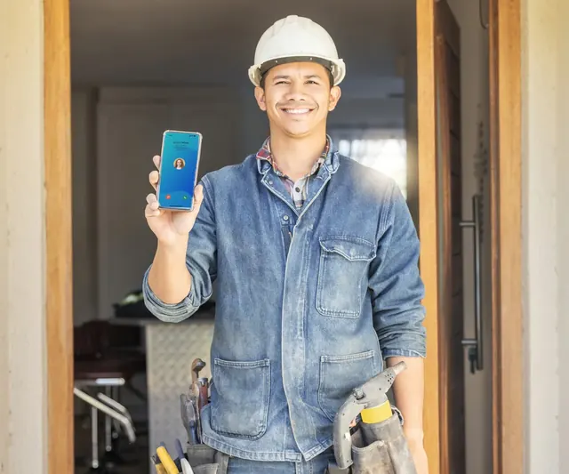 A smiling builder in a hard hat holding up his phone showing an incoming VOCPhone call